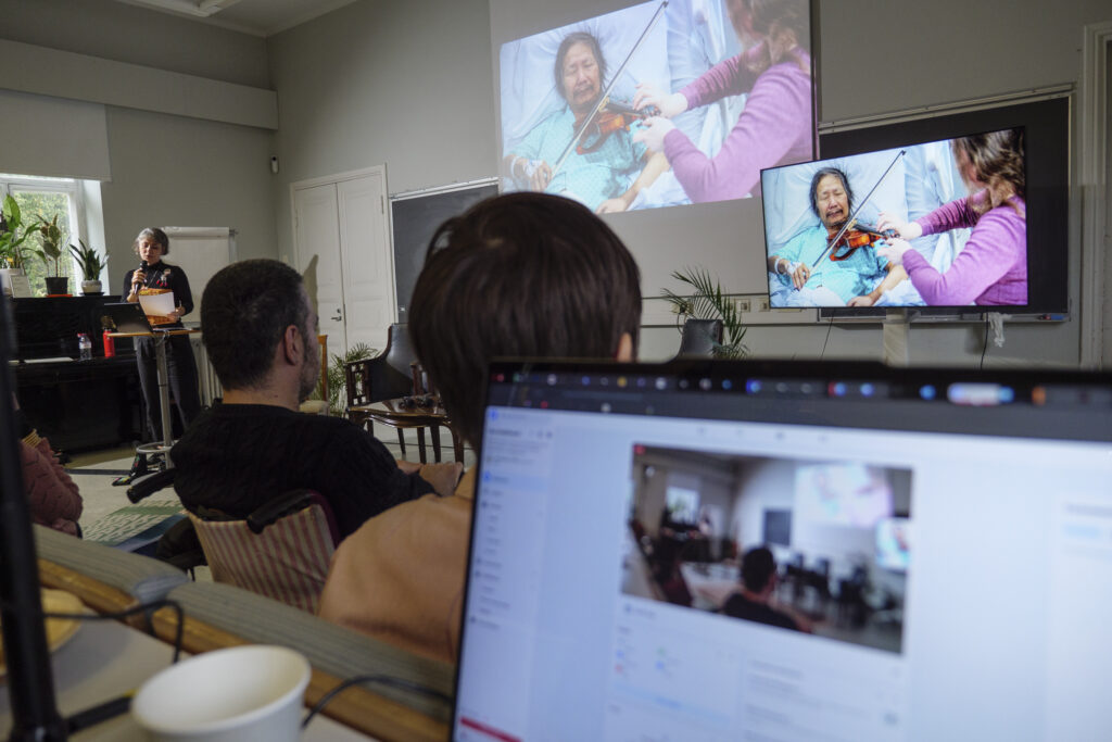 Audience watching an artist playing violin through a monitor and screening