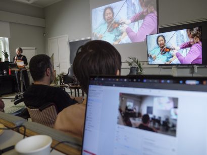 Audience watching an artist playing violin through a monitor and screening